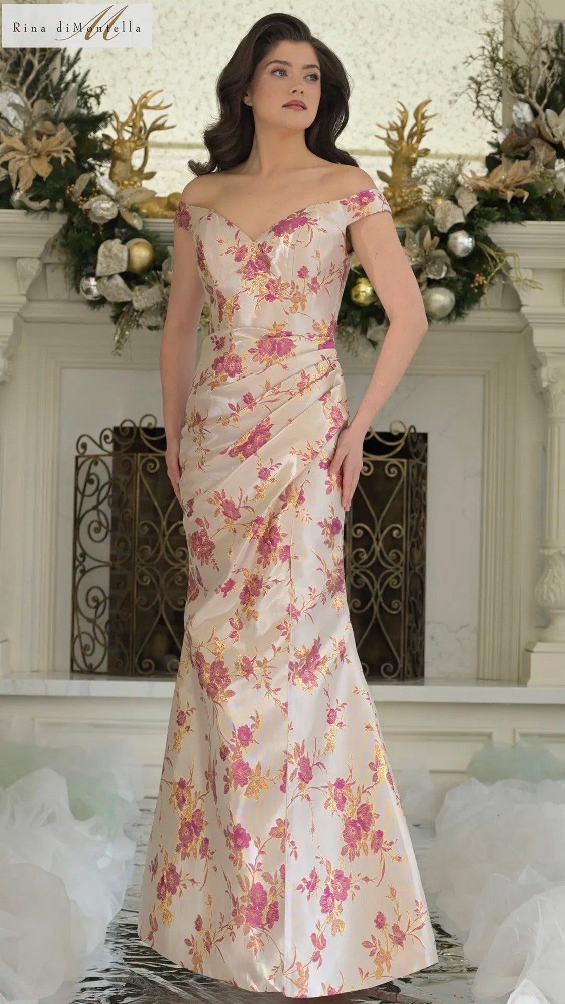 A woman stands indoors by a decorated fireplace wearing the Rina Di Montella RD3350 long formal dress in Pink Multi.